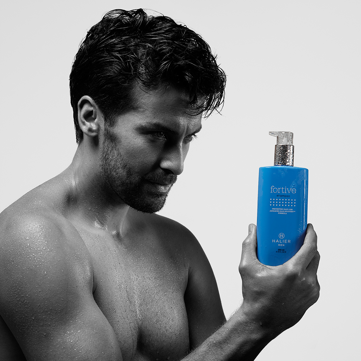 Black and white promotional image featuring a man holding a bottle of Hairvity hair care supplements.